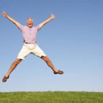 Senior man jumping in air with arms raised smiling